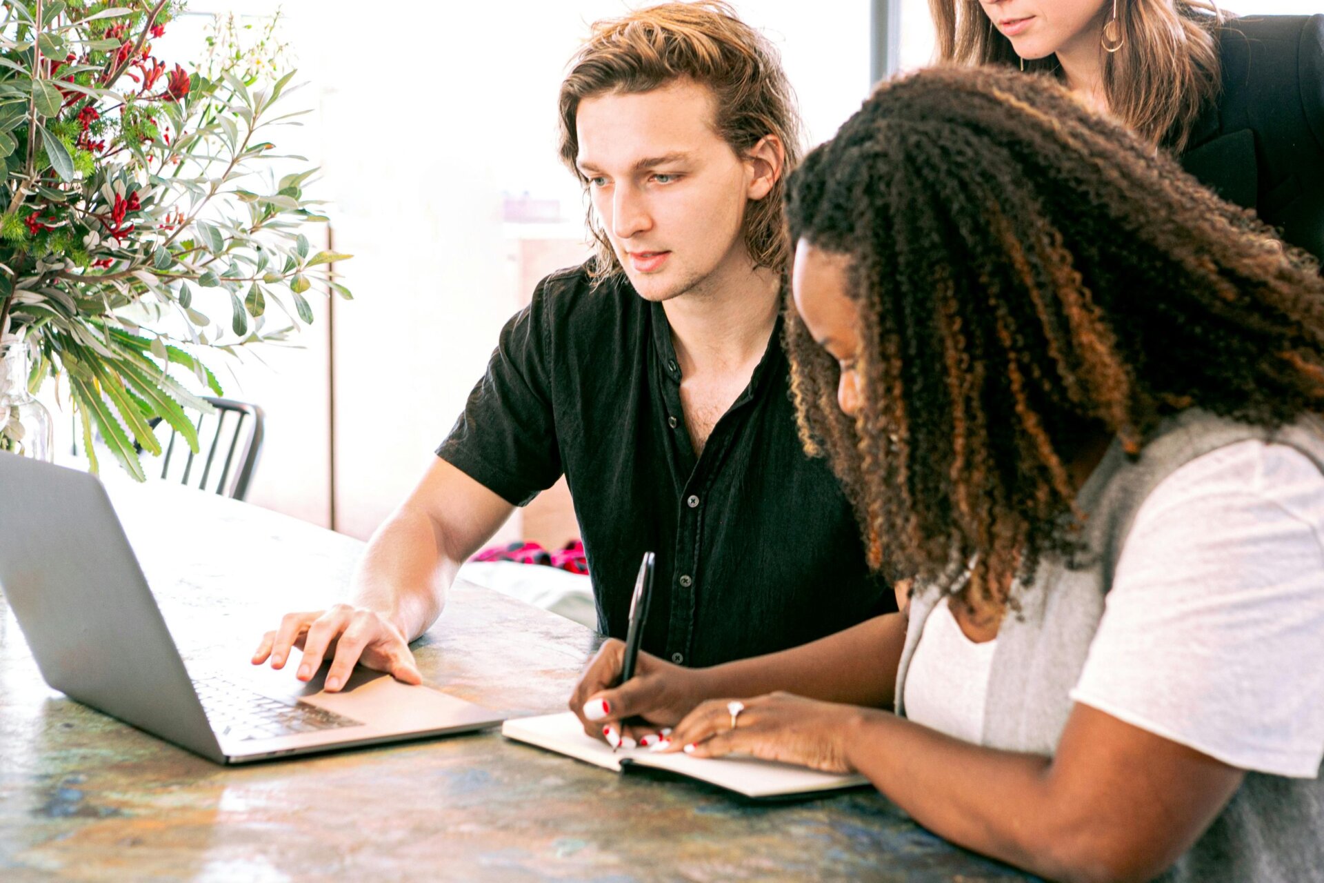 three people working together taking notes and looking at computer
