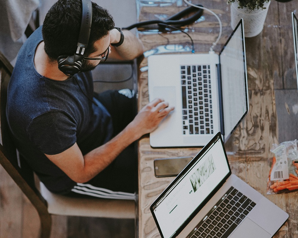 Person wearing headphones working on a laptop at a wooden desk.